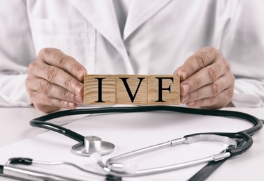 Image of In vitro fertilization. Doctor holding wooden cubes with abbreviation IVF above table, closeup
