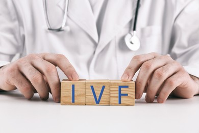 Image of In vitro fertilization. Doctor holding wooden cubes with abbreviation IVF at table, closeup