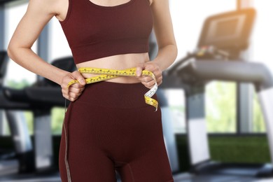 Image of Athletic woman with flat belly and measuring tape in gym, closeup