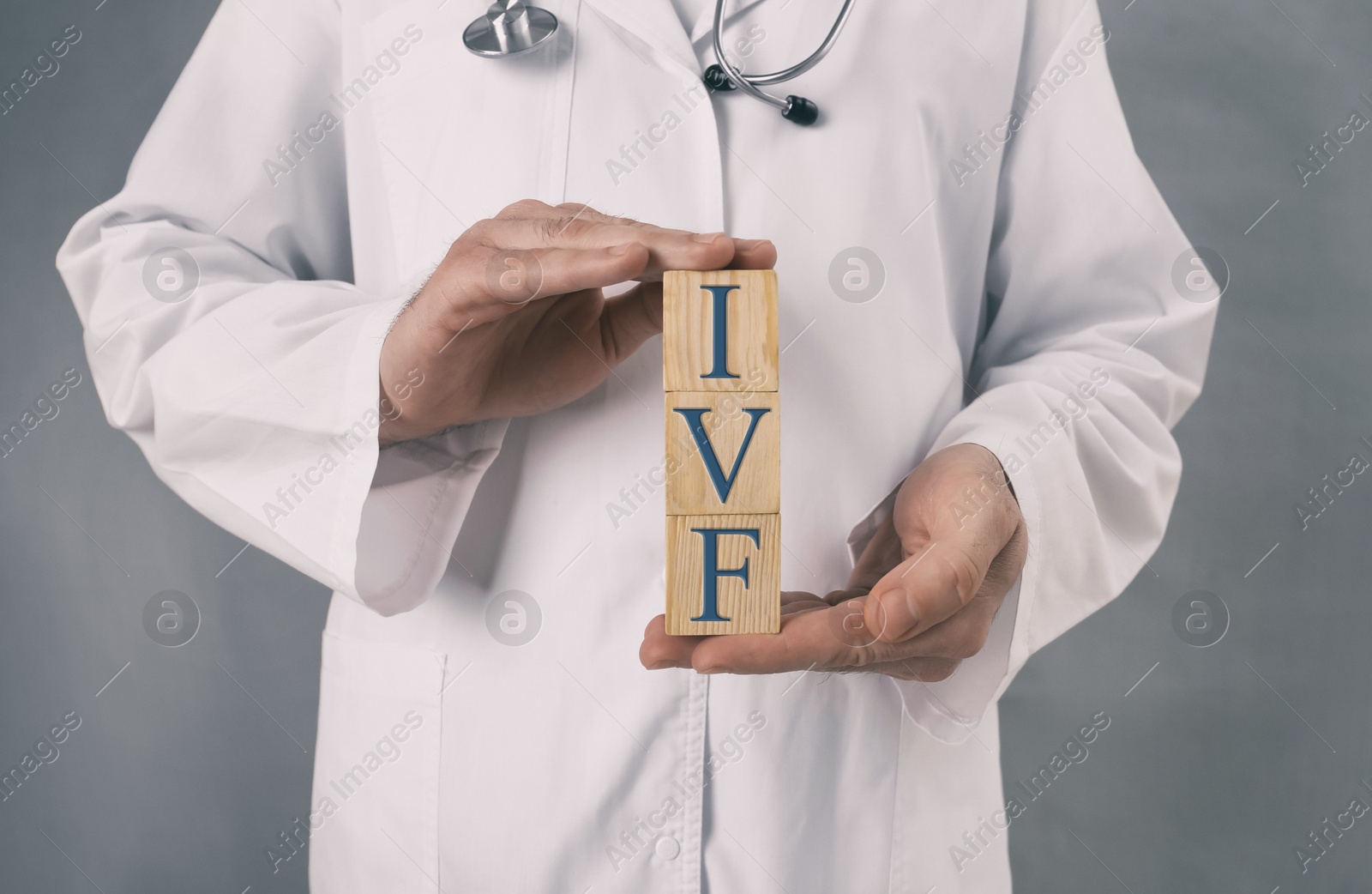Image of In vitro fertilization. Doctor holding wooden cubes with abbreviation IVF against grey background, closeup