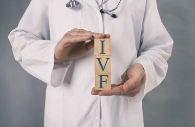 Image of In vitro fertilization. Doctor holding wooden cubes with abbreviation IVF against grey background, closeup