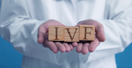 Image of In vitro fertilization. Doctor holding wooden cubes with abbreviation IVF against blue background, closeup. Banner design