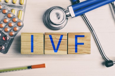 Image of In vitro fertilization. Wooden cubes with abbreviation IVF, pills, syringe and stethoscope on table, top view