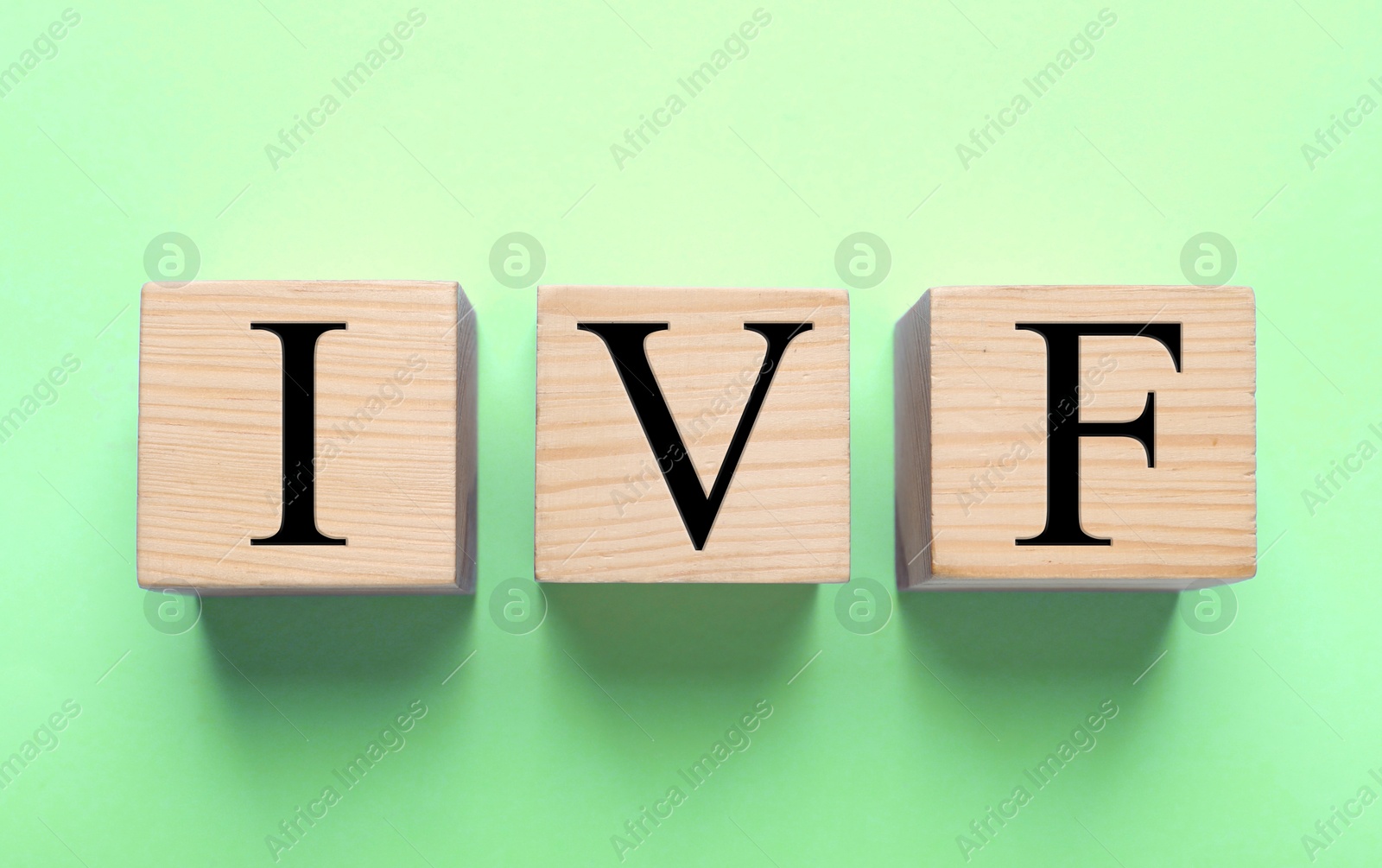 Image of In vitro fertilization. Wooden cubes with abbreviation IVF on light green background, top view. Banner design