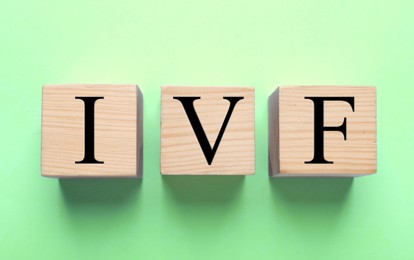 Image of In vitro fertilization. Wooden cubes with abbreviation IVF on light green background, top view. Banner design