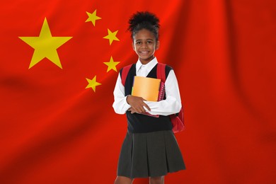 Image of Little girl with backpack and notebooks against flag of China. Language school