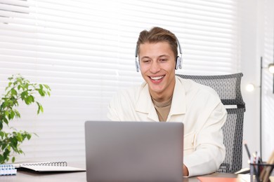 Photo of Man in headphones passing online test on laptop at table indoors