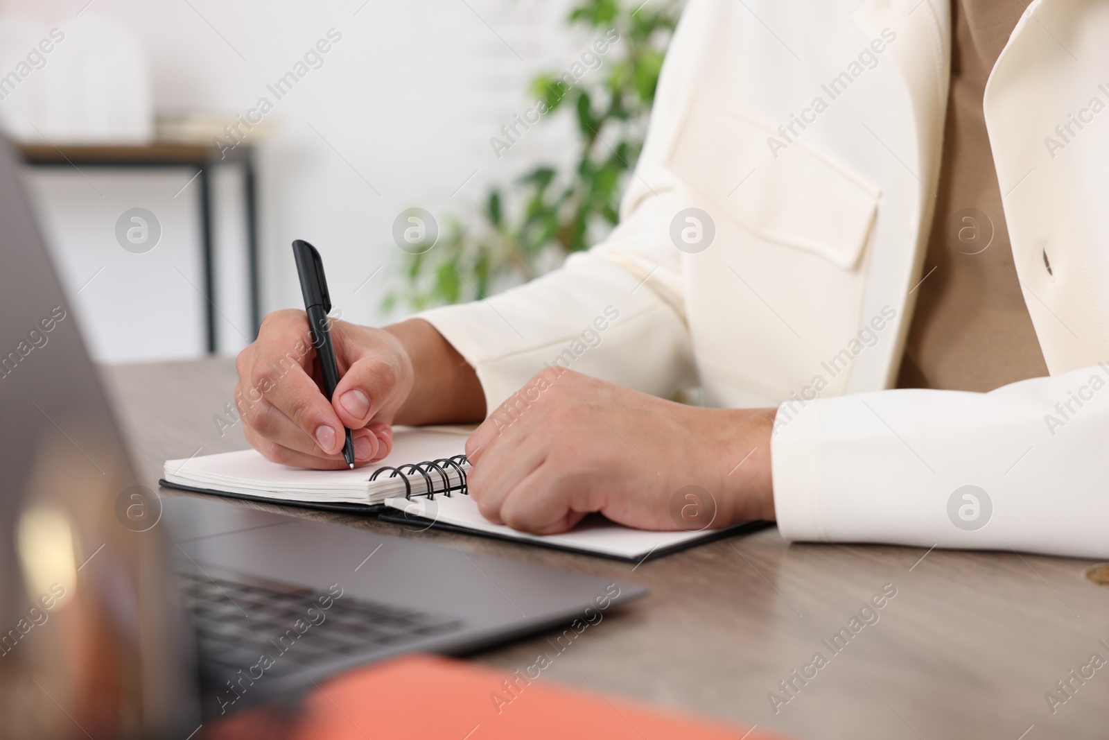 Photo of Man taking notes while passing online test via laptop at wooden table indoors, closeup