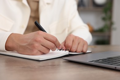 Photo of Man taking notes while passing online test via laptop at wooden table indoors, closeup