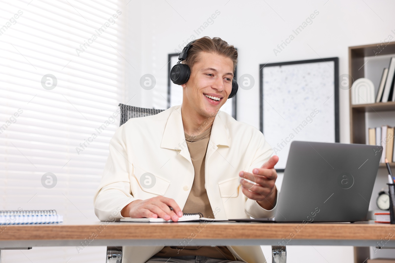 Photo of Man in headphones passing online test via laptop at table indoors