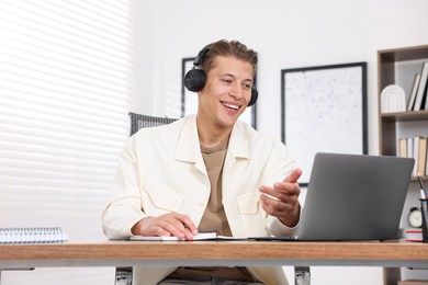 Photo of Man in headphones passing online test via laptop at table indoors