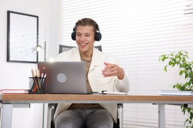 Photo of Man in headphones passing online test via laptop at table indoors
