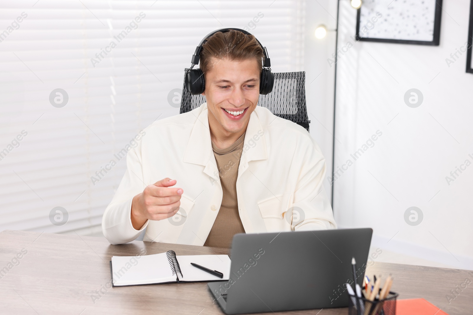 Photo of Man in headphones passing online test via laptop at table indoors