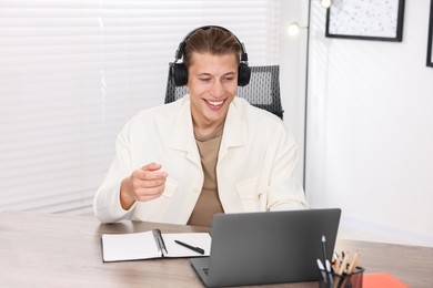 Photo of Man in headphones passing online test via laptop at table indoors