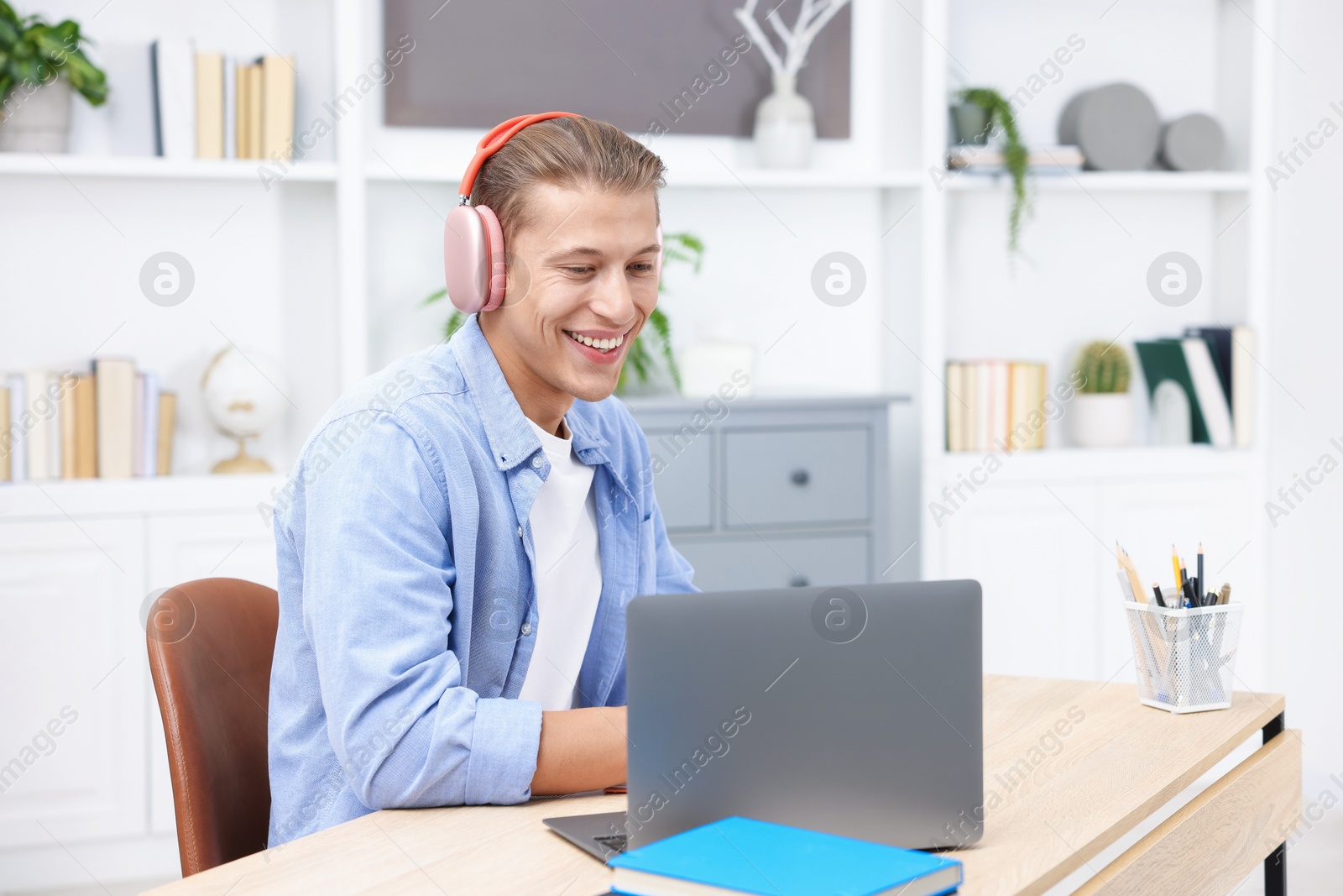 Photo of Man in headphones passing online test via laptop at table indoors
