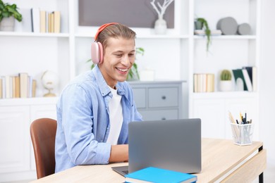 Photo of Man in headphones passing online test via laptop at table indoors
