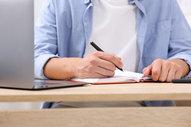 Photo of Man taking notes while passing online test via laptop at wooden table indoors, closeup
