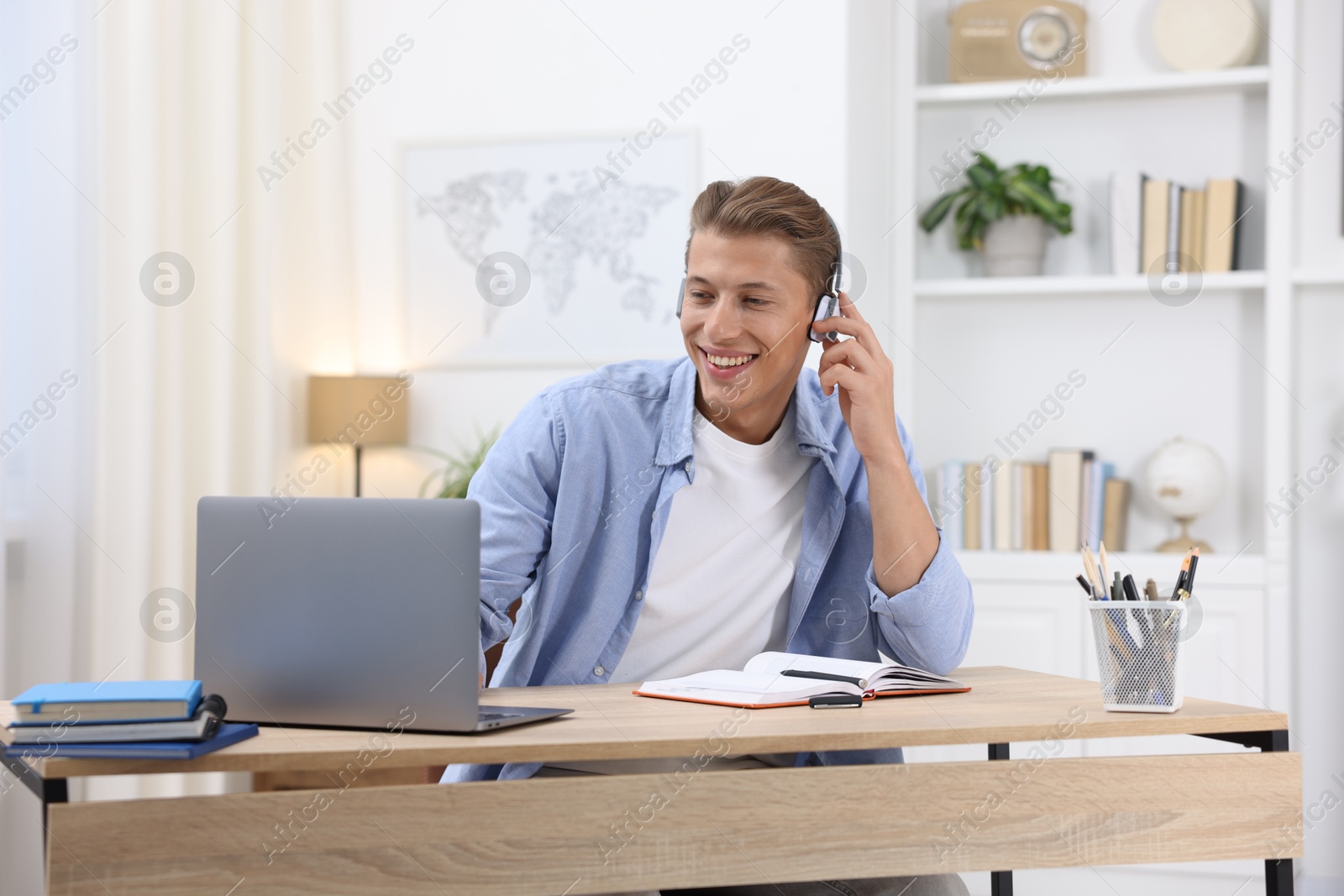 Photo of Man in headphones passing online test via laptop at table indoors