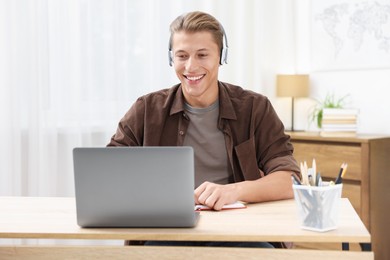 Photo of Man in headphones passing online test via laptop at table indoors