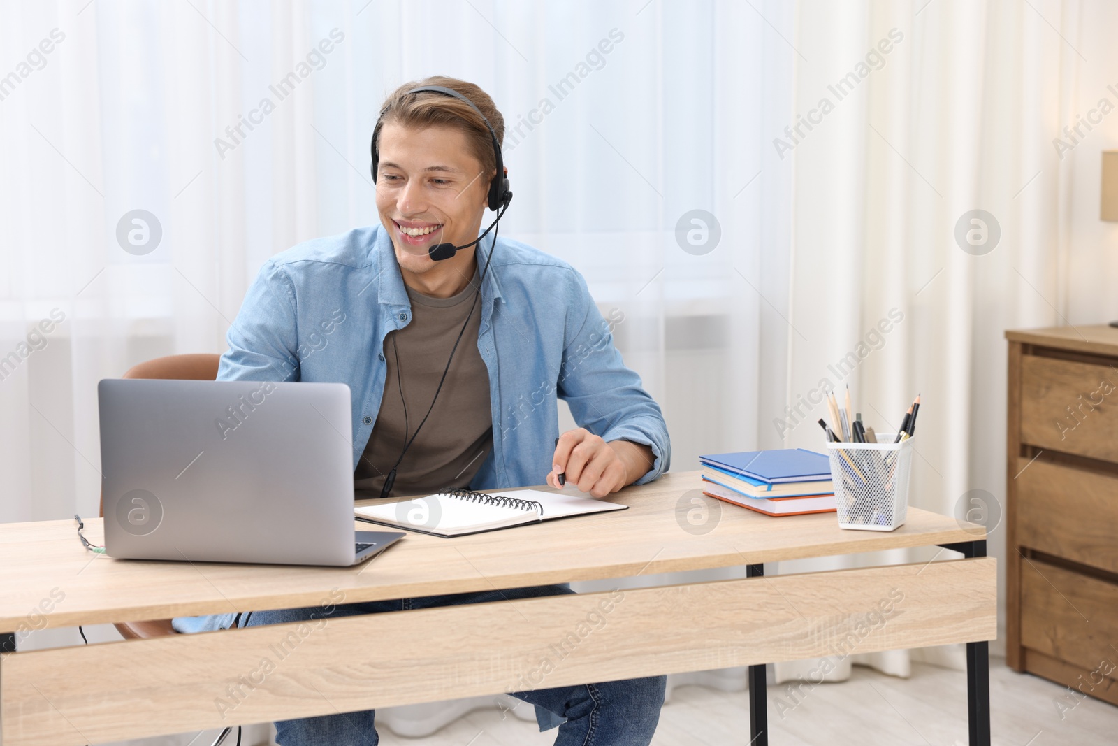 Photo of Man in headset passing online test via laptop at table indoors