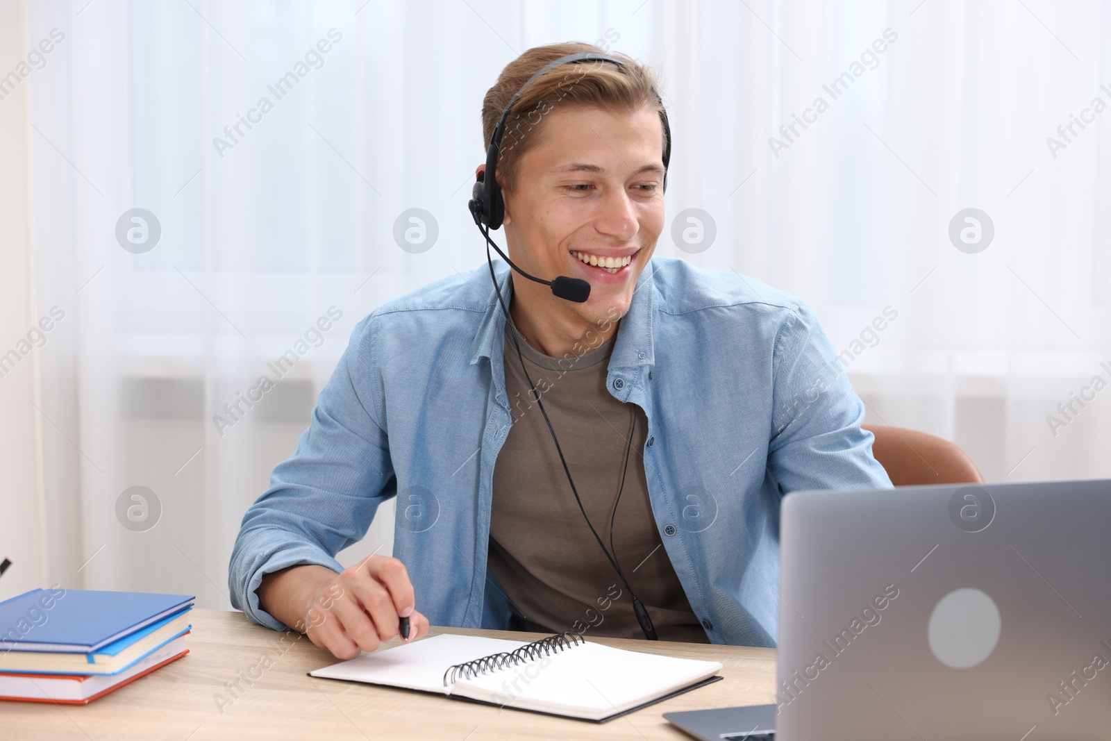 Photo of Man in headset passing online test via laptop at table indoors