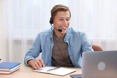 Photo of Man in headset passing online test via laptop at table indoors
