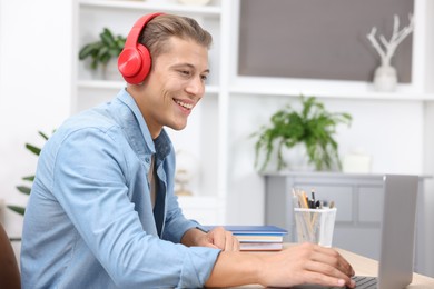 Photo of Man in headphones passing online test via laptop at table indoors