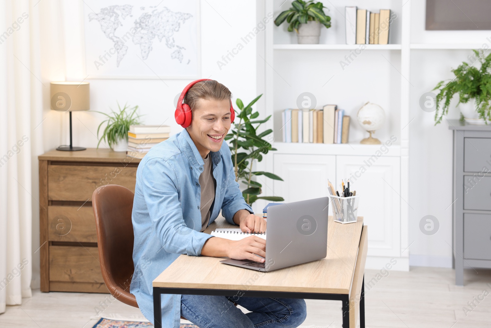 Photo of Man in headphones passing online test via laptop at table indoors