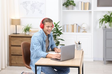 Photo of Man in headphones passing online test via laptop at table indoors