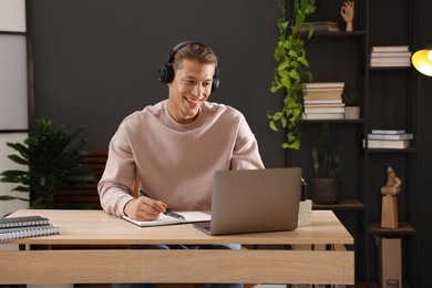 Photo of Man in headphones passing online test via laptop at table indoors