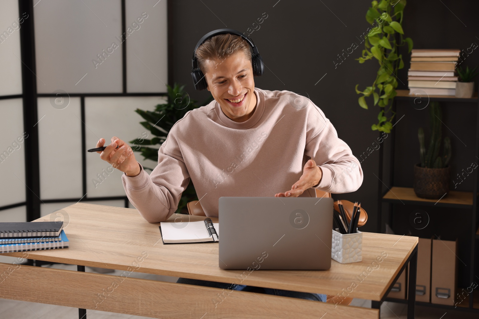 Photo of Man in headphones passing online test via laptop at table indoors