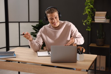 Photo of Man in headphones passing online test via laptop at table indoors