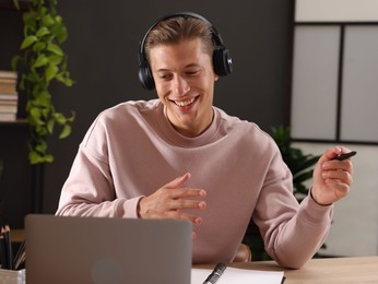 Photo of Man in headphones passing online test via laptop at table indoors