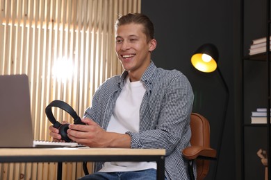 Photo of Man with headphones passing online test via laptop at table indoors