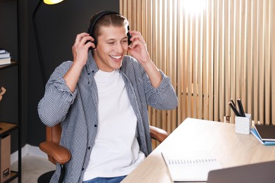 Photo of Man in headphones passing online test via laptop at table indoors