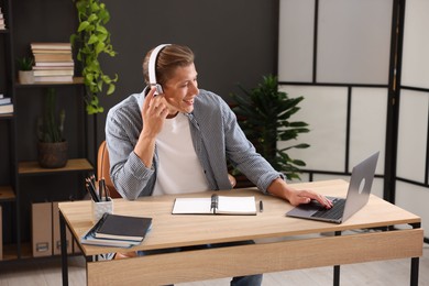 Photo of Man in headphones passing online test via laptop at table indoors