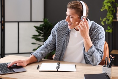 Photo of Man in headphones passing online test via laptop at table indoors