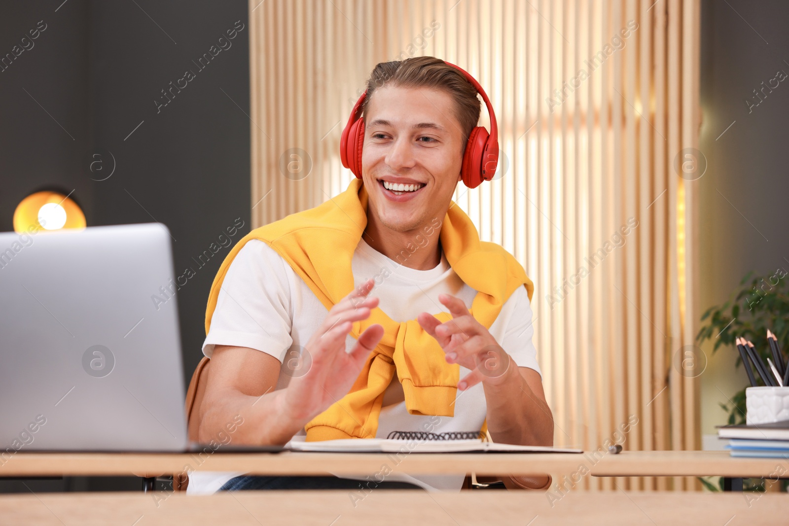 Photo of Man in headphones passing online test via laptop at table indoors