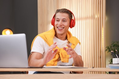 Photo of Man in headphones passing online test via laptop at table indoors