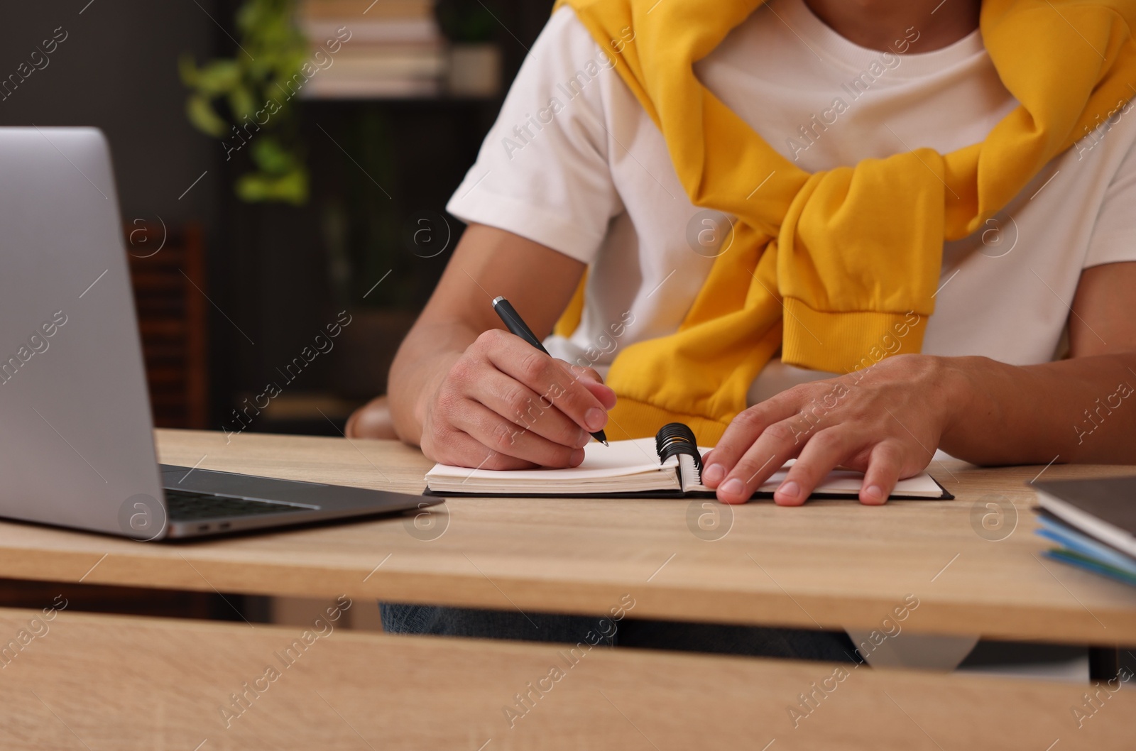 Photo of Man taking notes while passing online test via laptop at table indoors, closeup