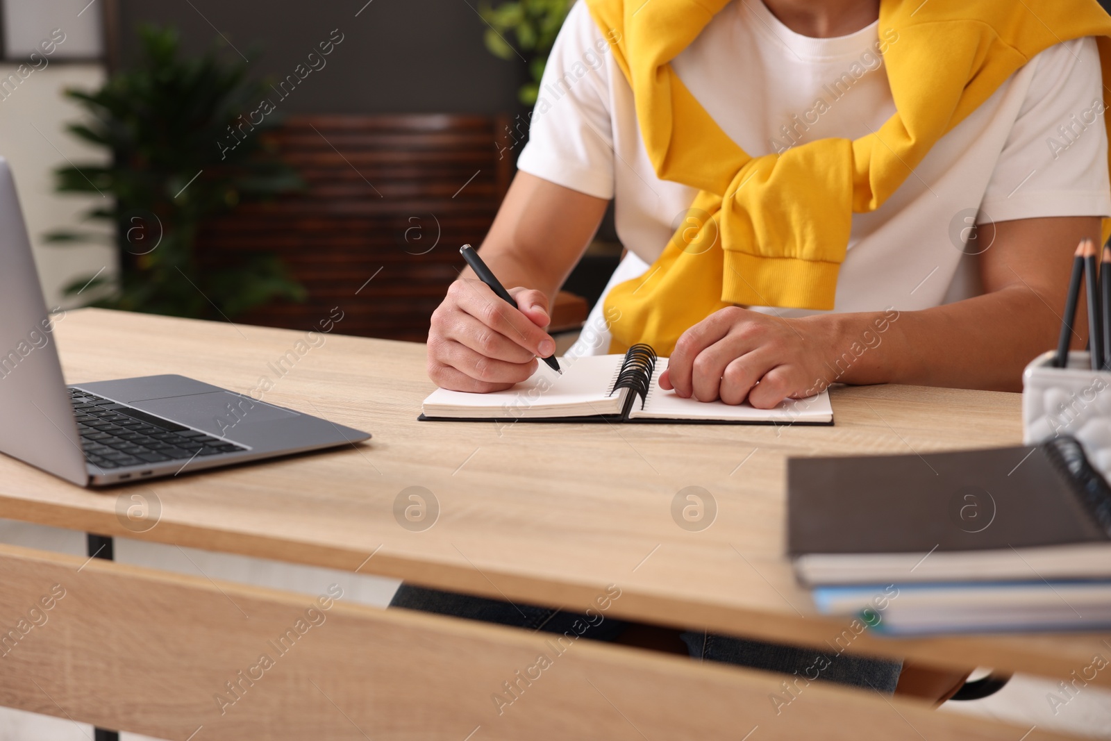 Photo of Man taking notes while passing online test via laptop at table indoors, closeup