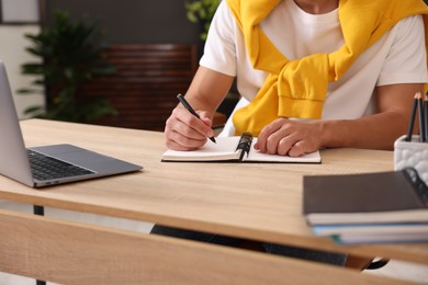 Photo of Man taking notes while passing online test via laptop at table indoors, closeup