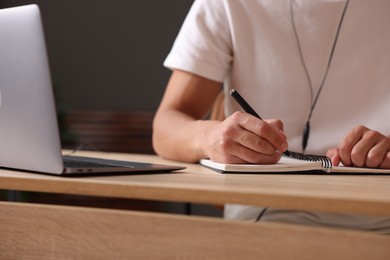 Photo of Man taking notes while passing online test via laptop at table indoors, closeup