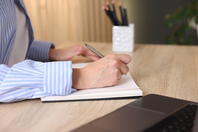 Photo of Woman taking notes while passing online test via laptop at table indoors, closeup