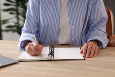Photo of Woman taking notes while passing online test via laptop at table indoors, closeup