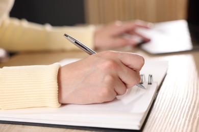 Photo of Woman taking notes while passing online test via laptop at table indoors, closeup