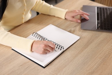 Photo of Woman taking notes while passing online test via laptop at table indoors, closeup