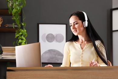 Photo of Woman in headphones passing online test via laptop at table indoors