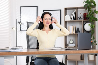 Photo of Woman in headphones passing online test via laptop at table indoors