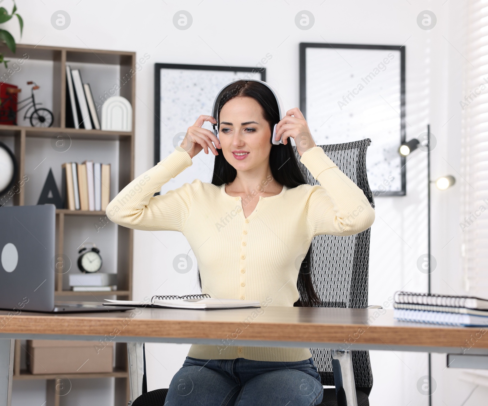Photo of Woman in headphones passing online test via laptop at table indoors